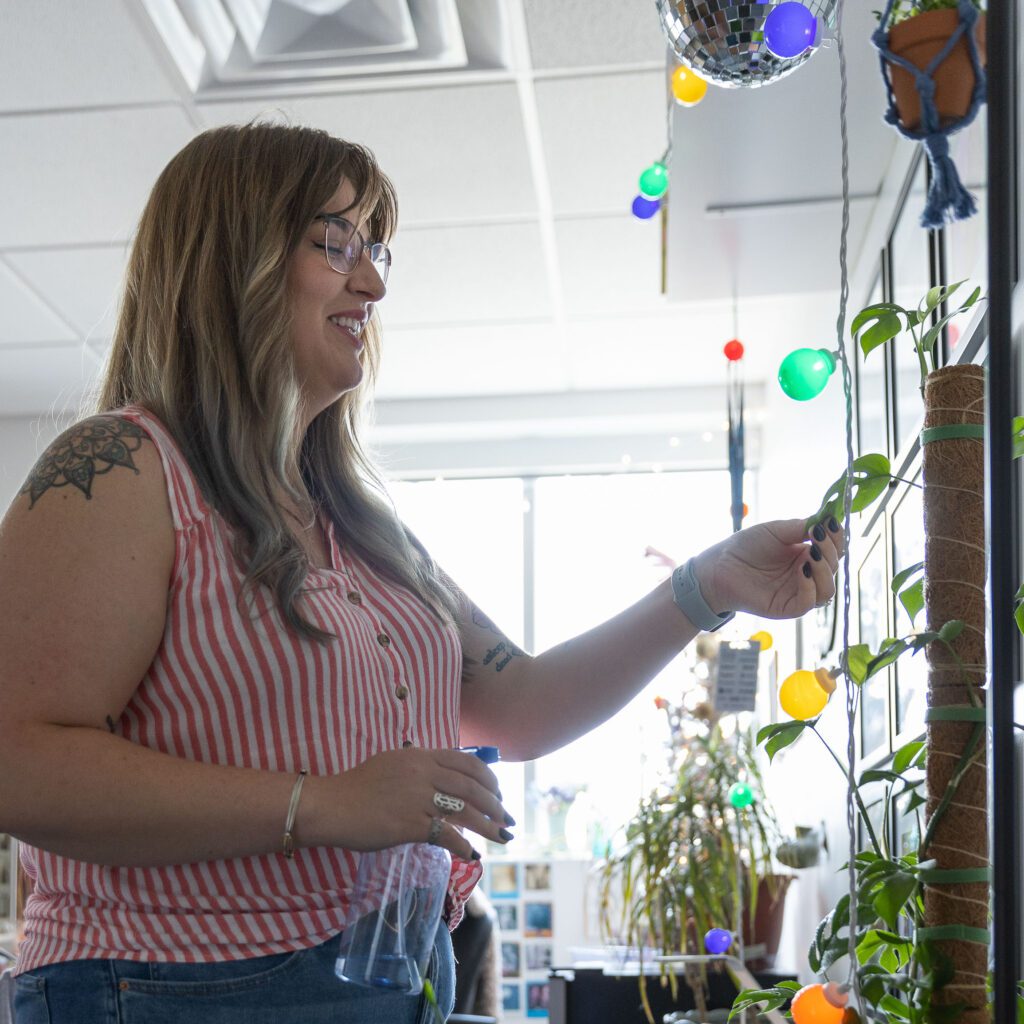 woman with a spray bottle misting a plant climbing up a pole
