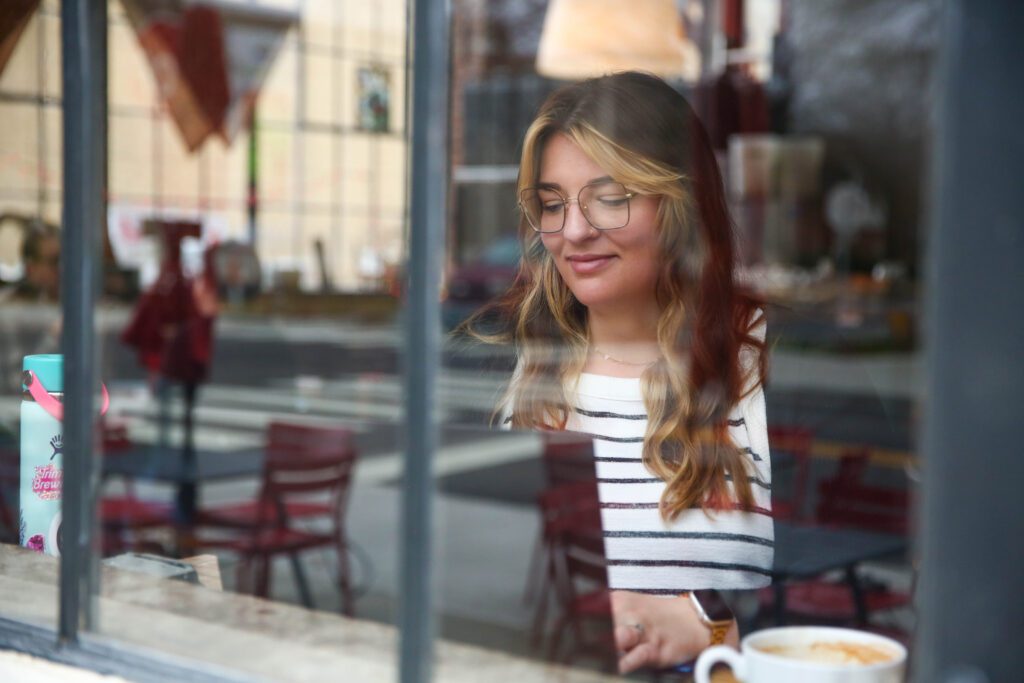 shot is through a window and shows a woman looking down at her laptop