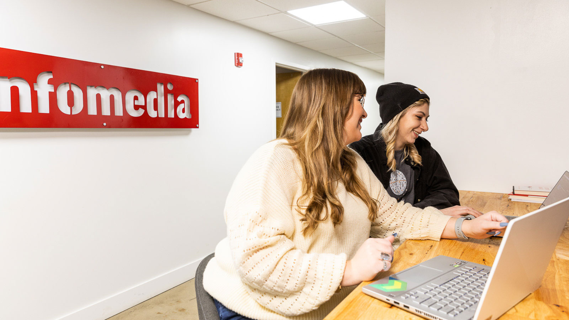 two smiling women sitting at a table working on laptops together